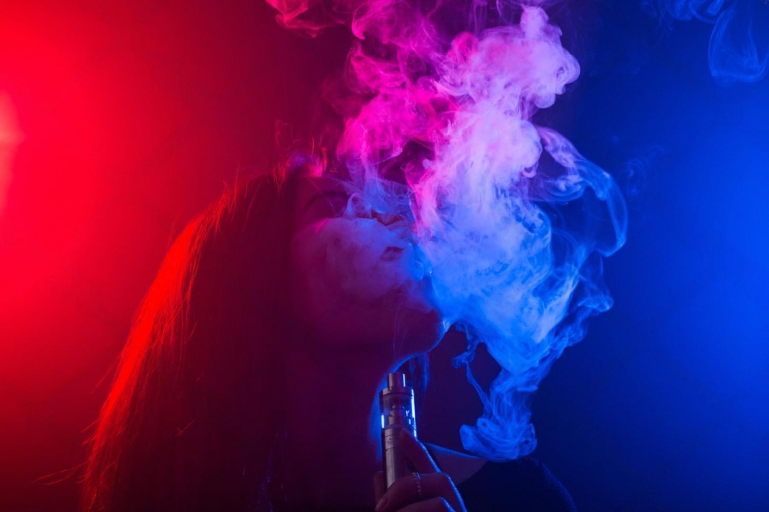 Close-up of a person using a refillable pod vape device with visible vapour clouds